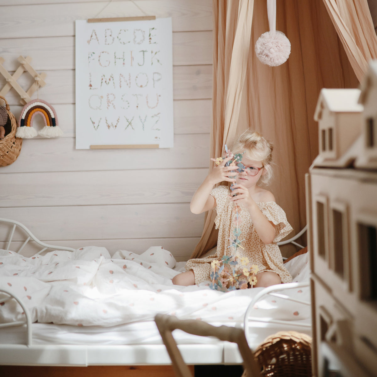 Girl plays on bed with mushie HEX Connect Building Toy Set in cozy, softly lit bedroom.