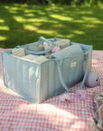 Mushie Changing Pad Liners in a light blue organizer on a pink picnic blanket outdoors.