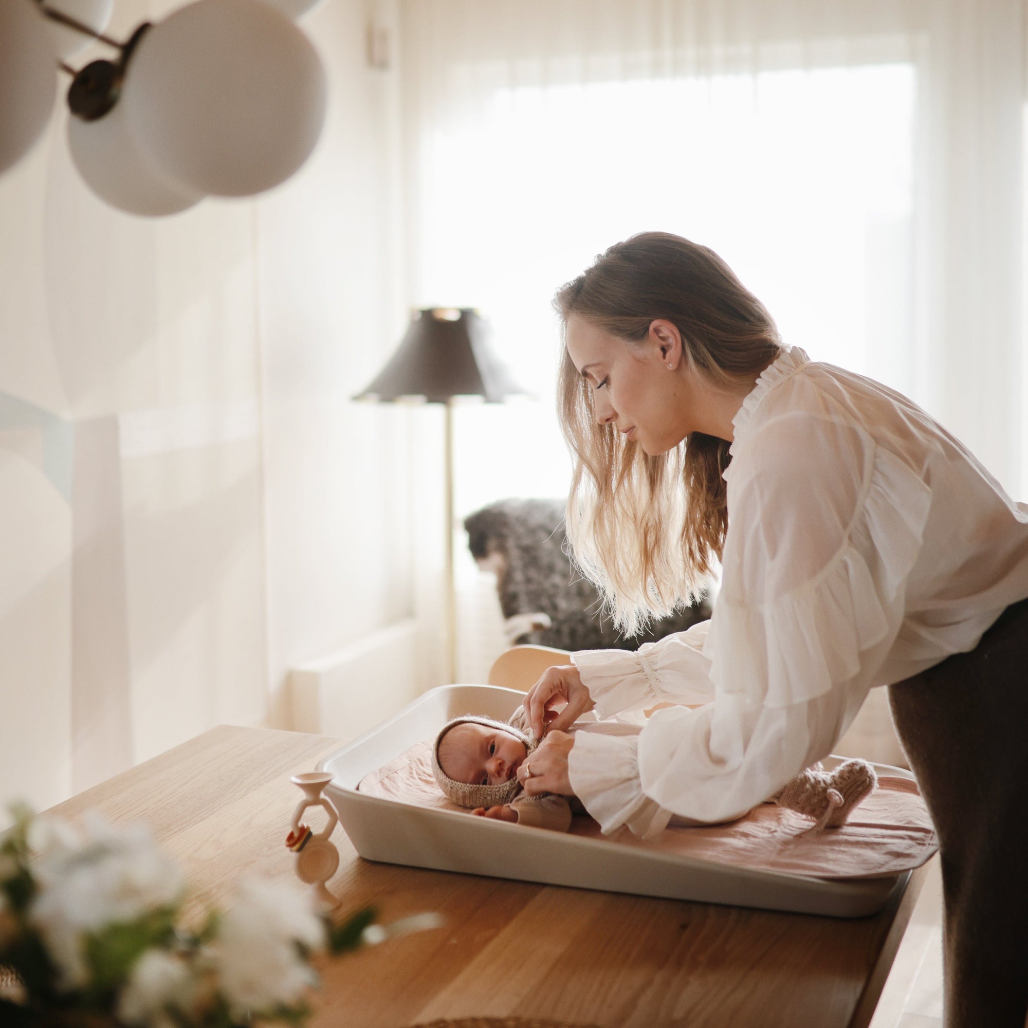 A woman uses Mushie Changing Pad Liners to change a baby’s diaper on a table.