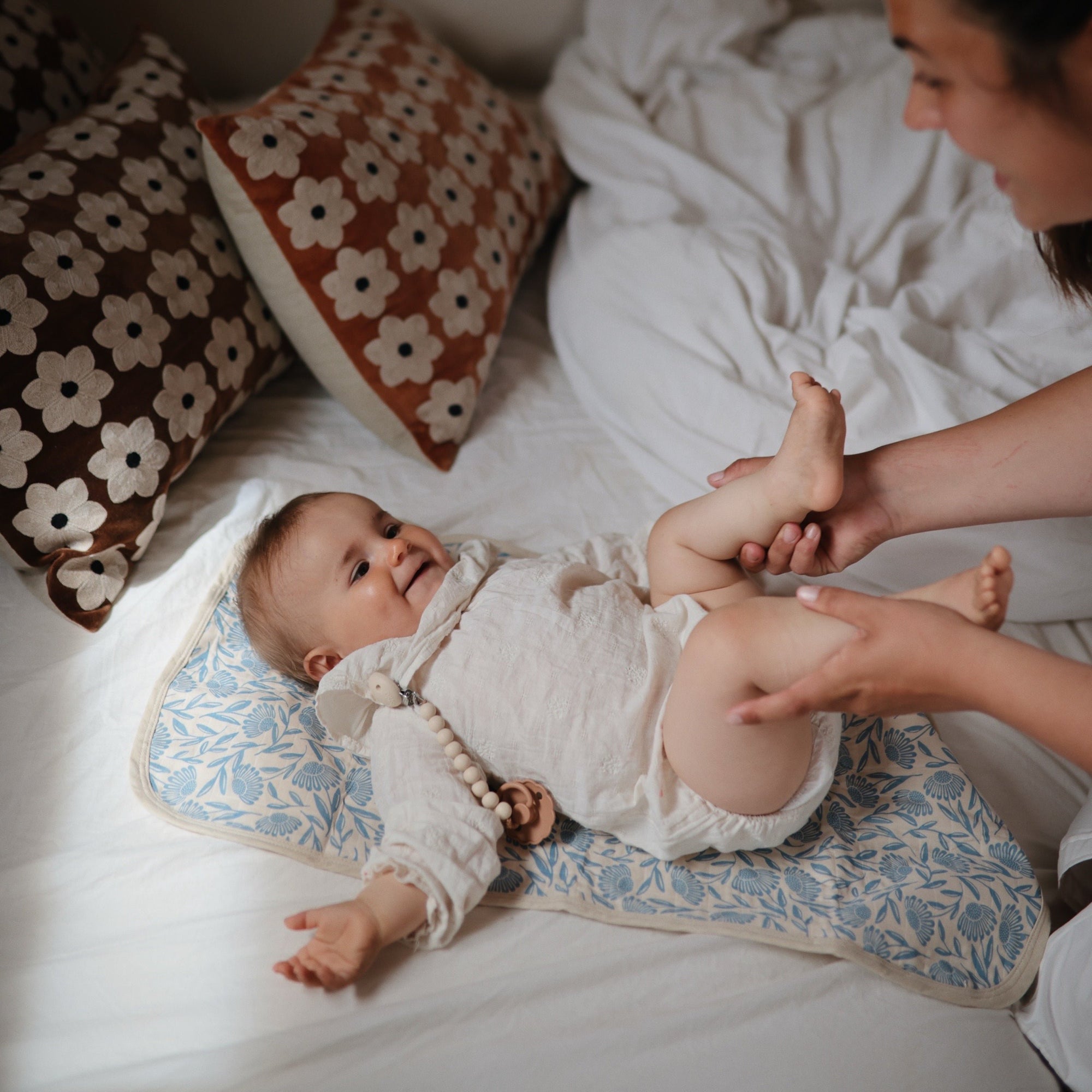 Baby smiles on mat using Mushie Changing Pad Liners as adult gently holds their legs nearby.