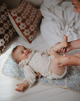 Baby smiles on mat using Mushie Changing Pad Liners as adult gently holds their legs nearby.