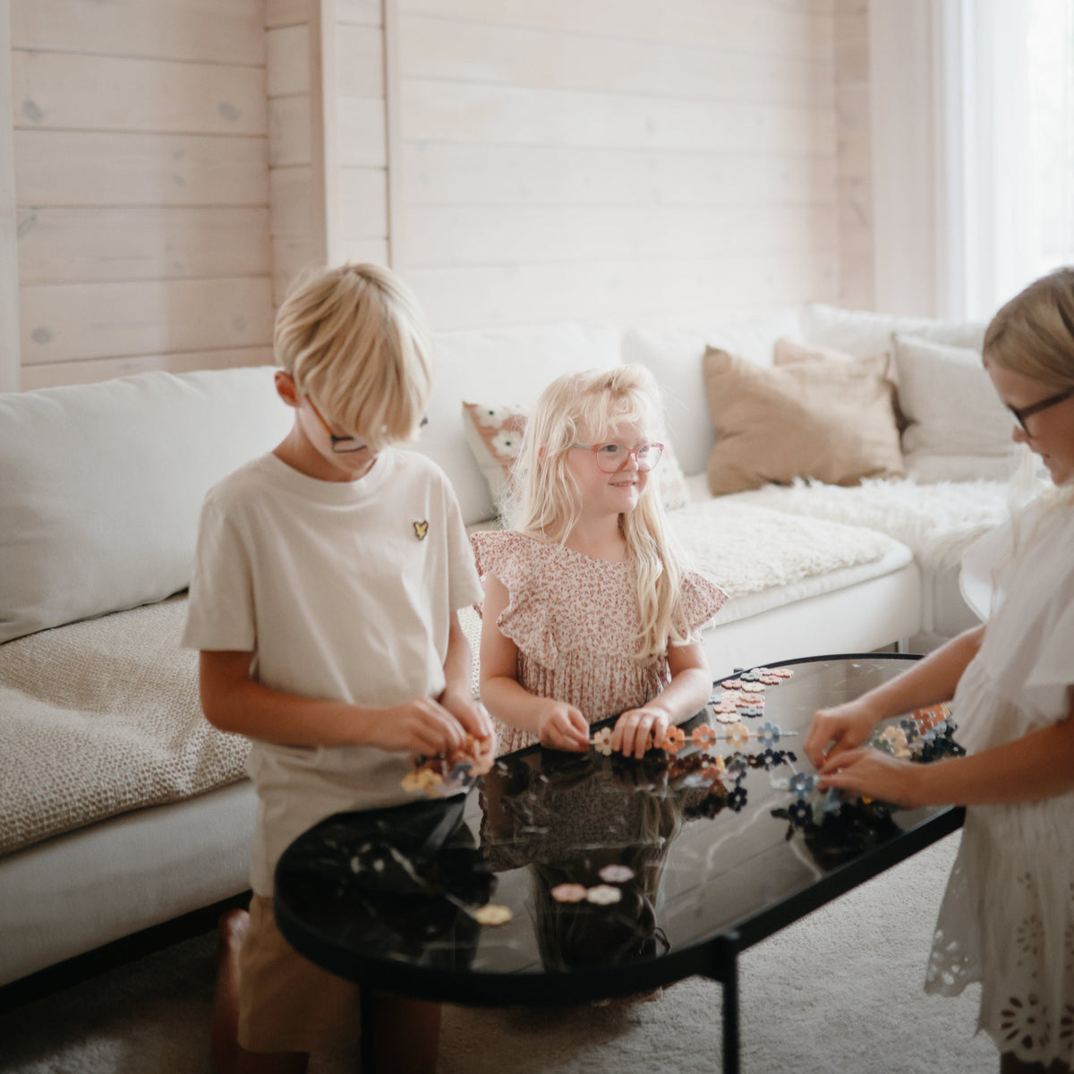 Three kids play with the mushie HEX Connect Building Toy Set on a black coffee table.