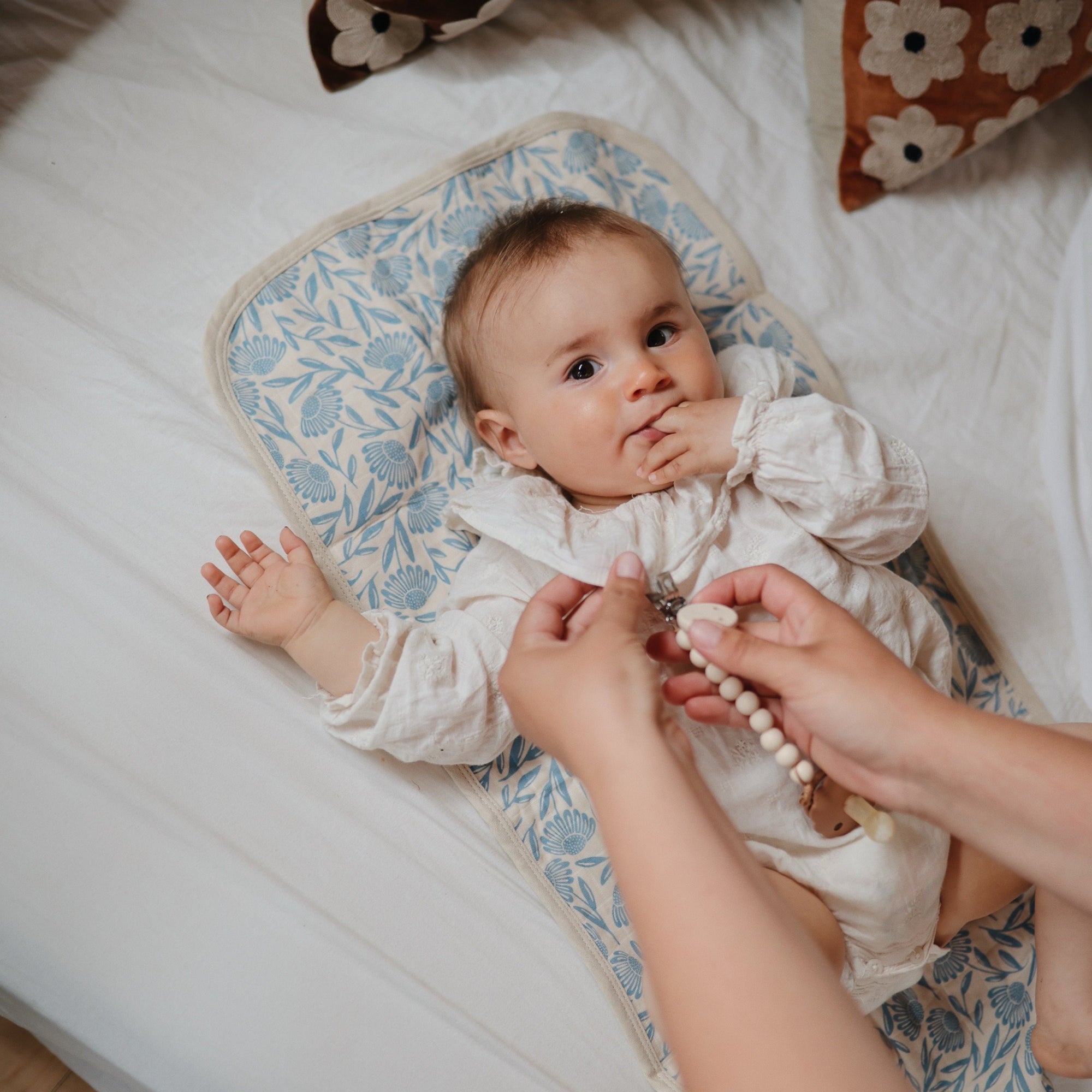 Baby on Mushie Changing Pad Liners, reaching for a beaded pacifier clip on patterned mat.