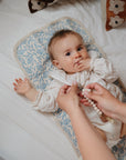 Baby on Mushie Changing Pad Liners, reaching for a beaded pacifier clip on patterned mat.