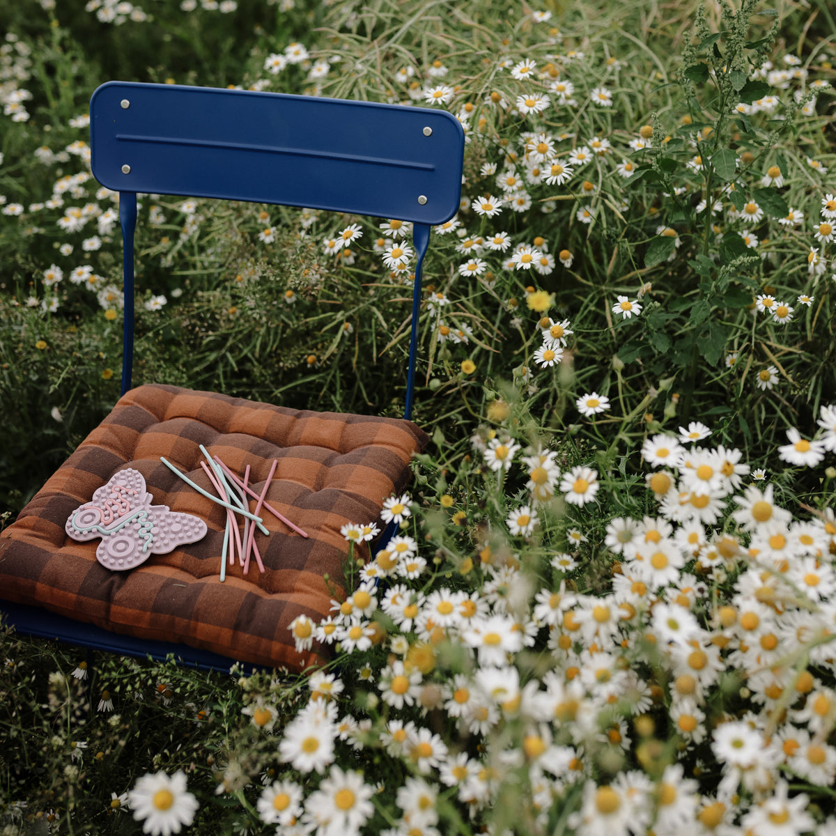 Blue chair with daisies, brown cushion, colored pencils, and mushie Silicone Sensory Toy on seat.
