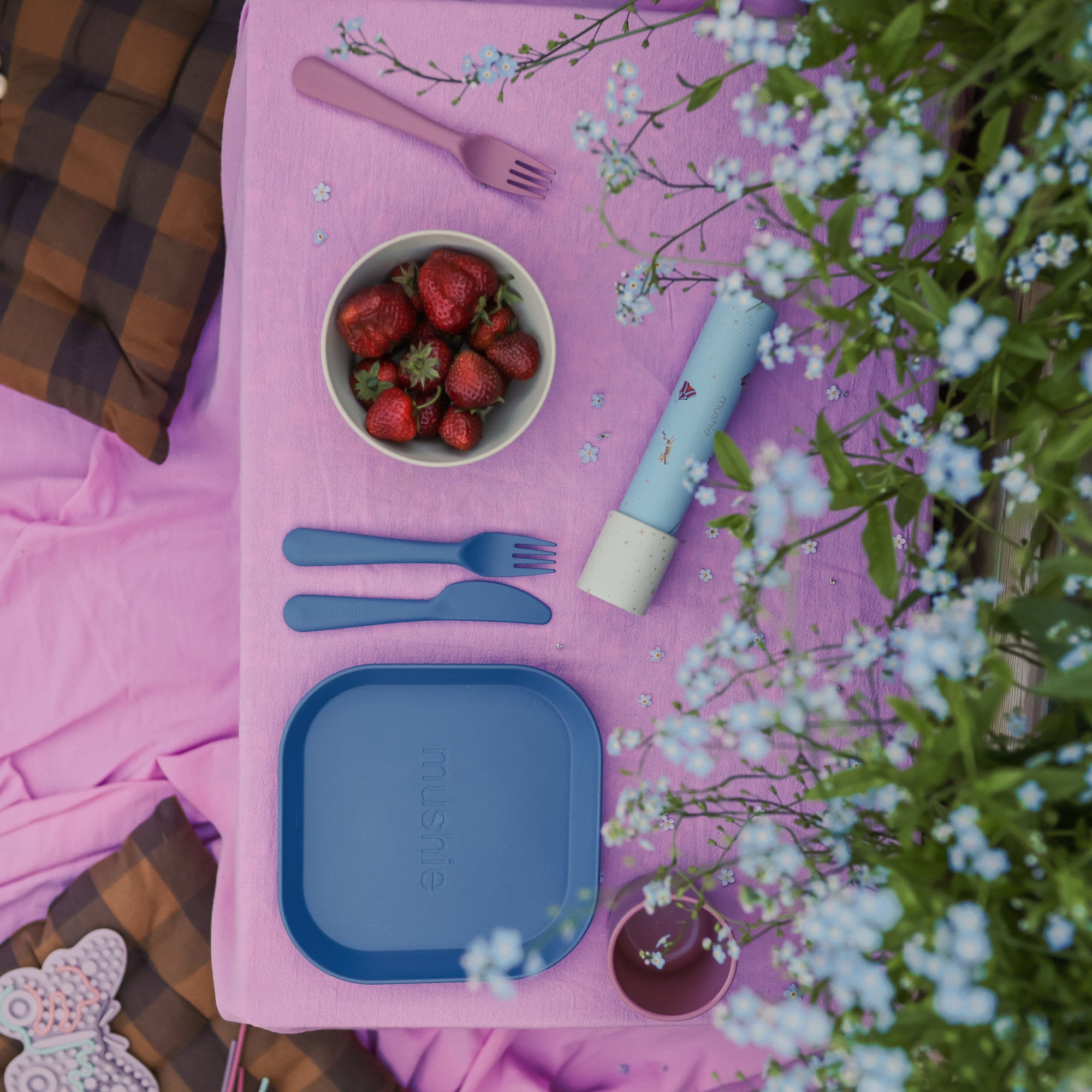 A picnic with strawberries, flowers, and a mushie Round Dinnerware Bowl on a pink cloth.