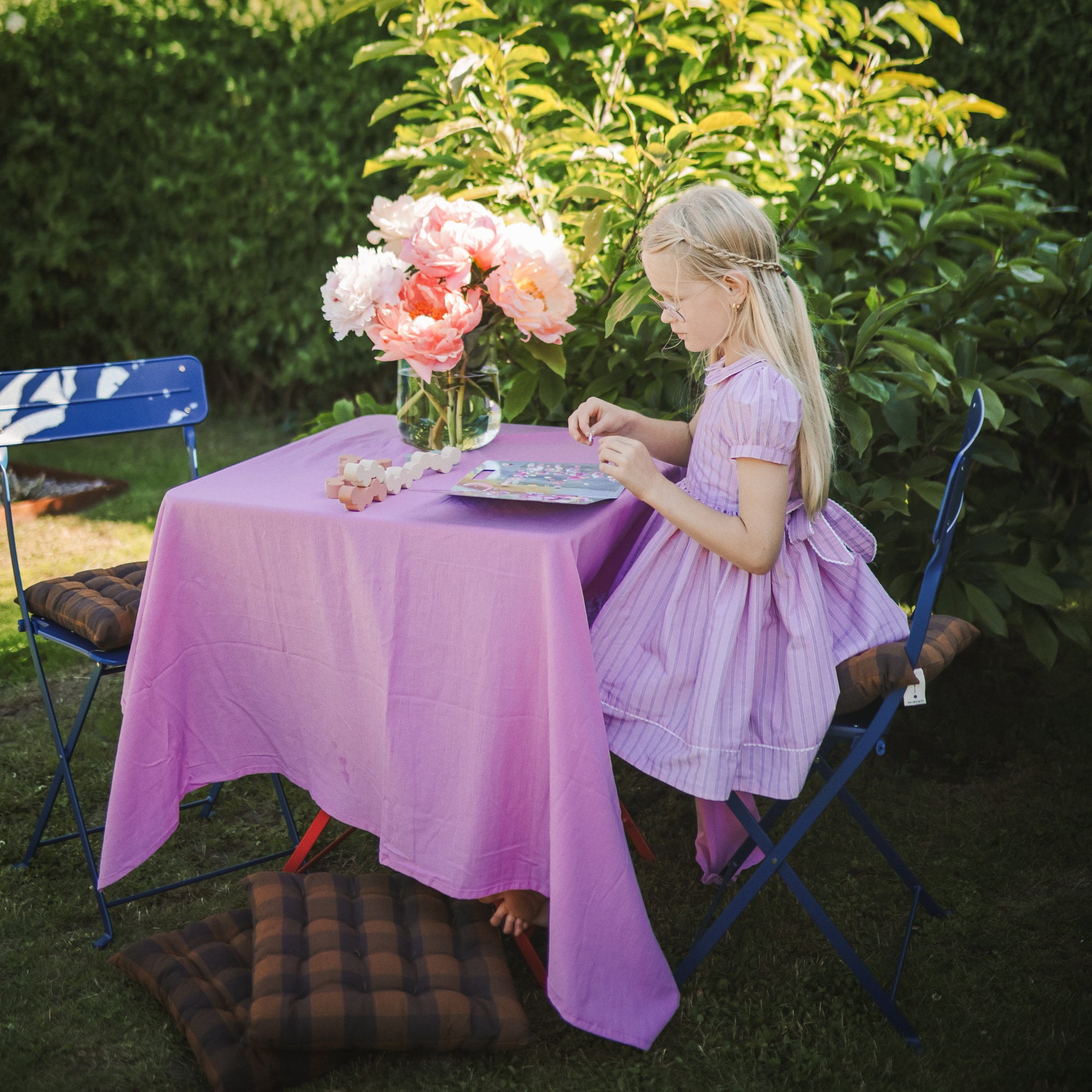A girl uses the mushie Reusable Sticker Set at a purple table outdoors.