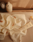Mushie Baby Cream and a pacifier on a beige surface with a cream floral baby blanket.