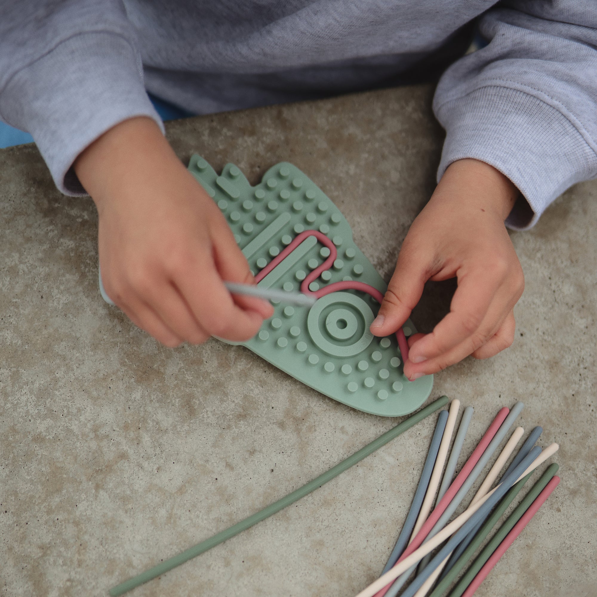 Child threads colorful sticks through mushie Silicone Sensory Toy for fine motor play.