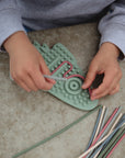 Child threads colorful sticks through mushie Silicone Sensory Toy for fine motor play.
