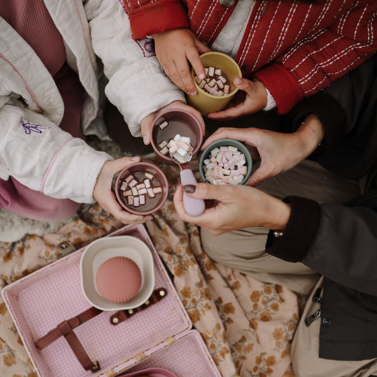 Four people holding colorful mushie Dinnerware Cups filled with hot cocoa and marshmallows.