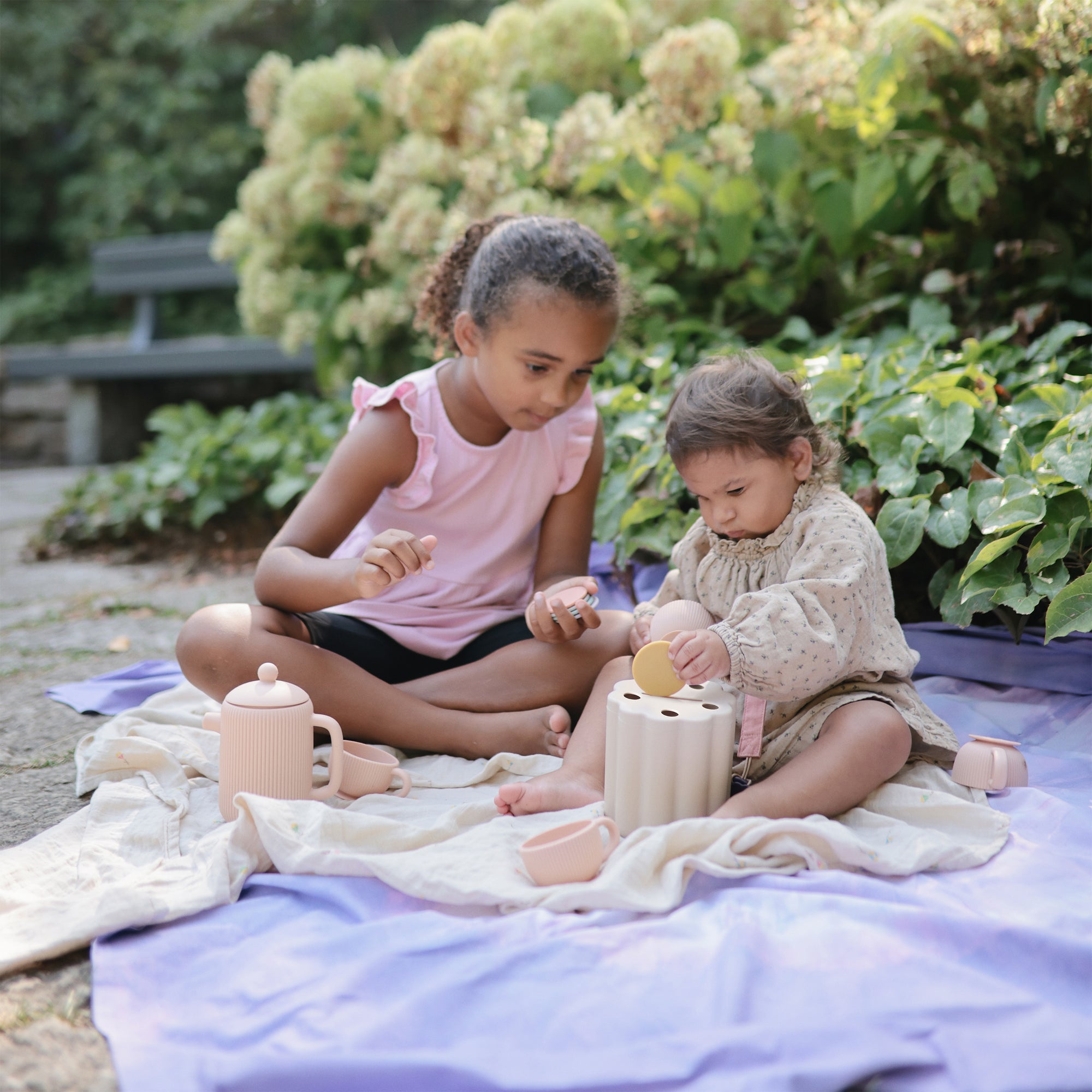 Two kids play outdoors with the mushie Coin &amp; Tube Sorting Set, building fine motor skills.