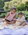 Two kids play outdoors with the mushie Coin & Tube Sorting Set, building fine motor skills.