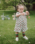Toddler with mushie Linen Pacifier Clip 2-Pack holds pacifier while playing outdoors.