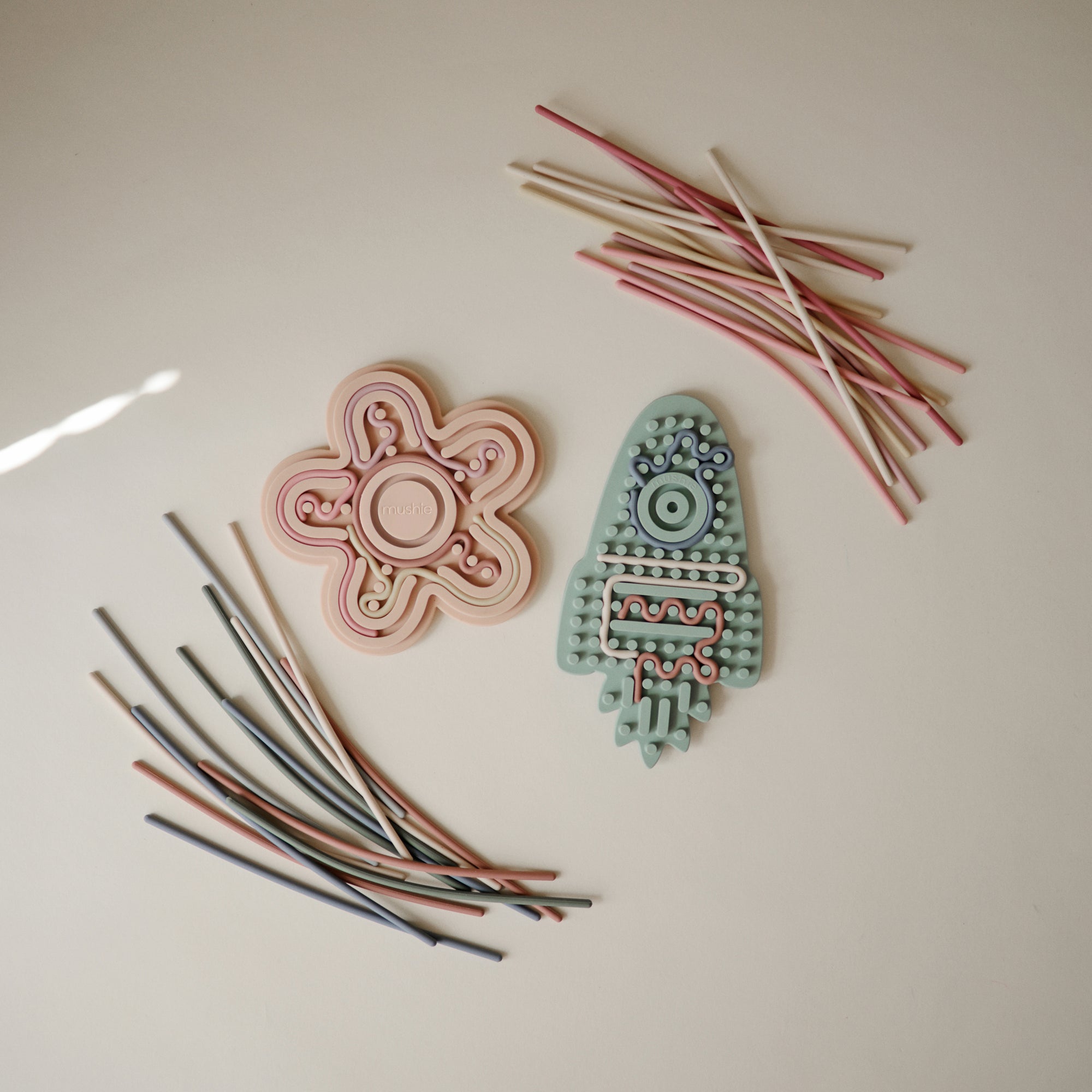 Two mushie Silicone Sensory Toys with colorful sticks, ideal for fine motor play on light surfaces.