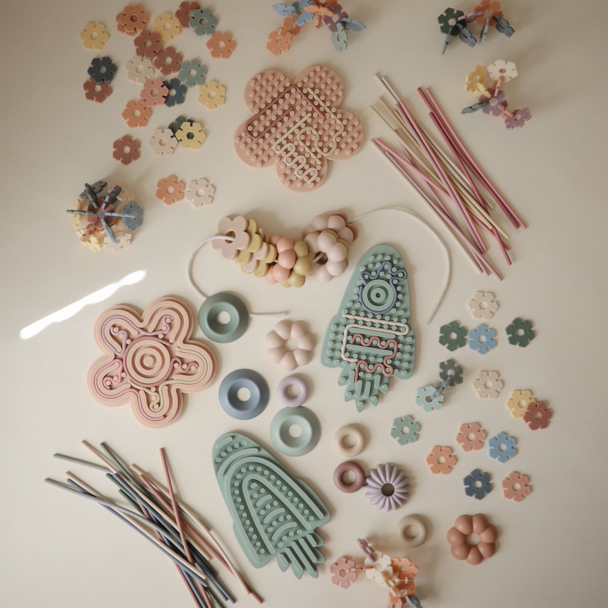 Mushie Silicone Sensory Toy with beads and strings for fine motor play on a light surface.
