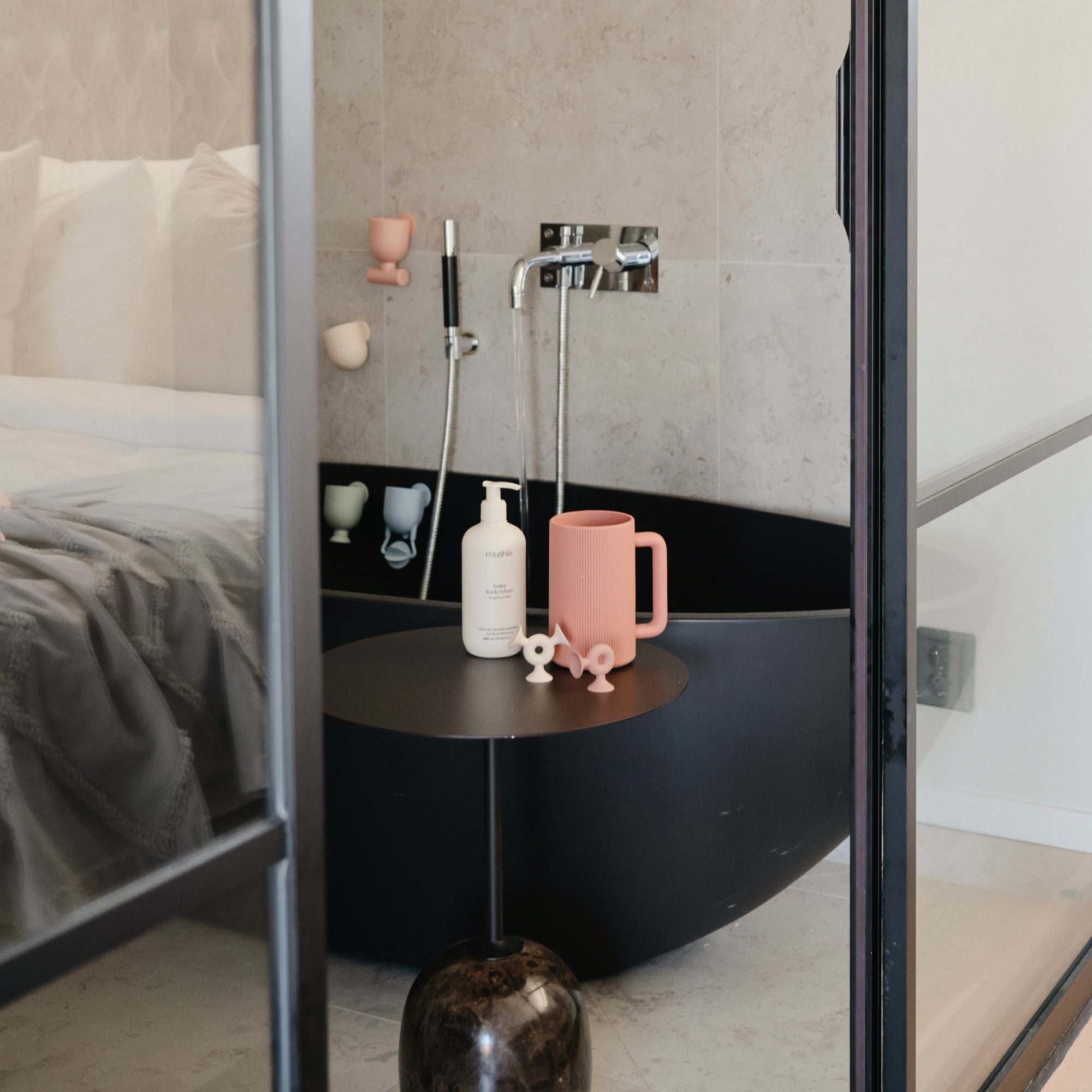 Modern black bathtub with mushie Baby Shampoo &amp; Body Wash beside a bed in a cozy room.