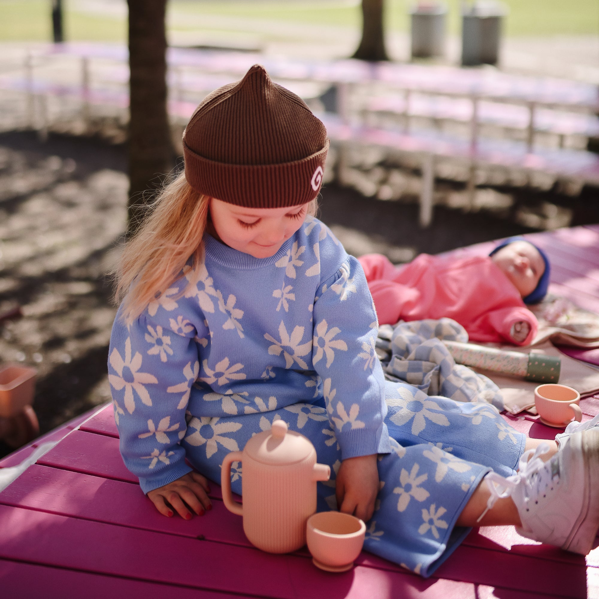Young child enjoys pretend play with Mushie Silicone Tea Play Set on a pink bench.