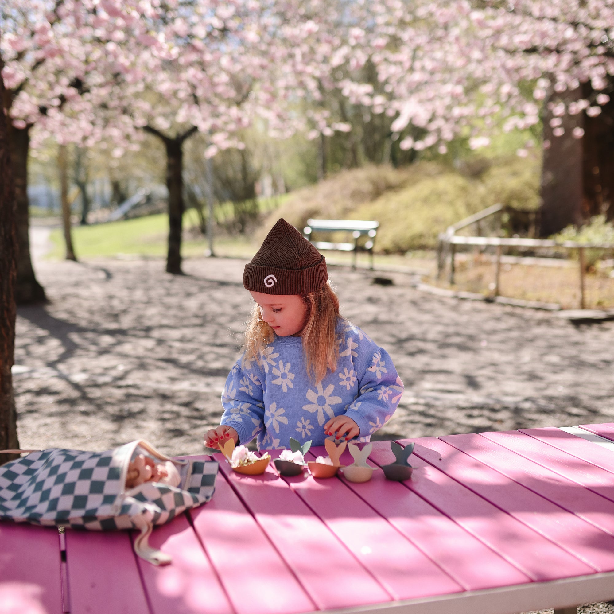 A child plays with toys near a mushie Water Resistant Wet Bag under cherry blossoms.