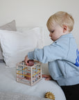 Toddler plays with mushie Elastic Shape Sorter, building fine motor skills by the bed.