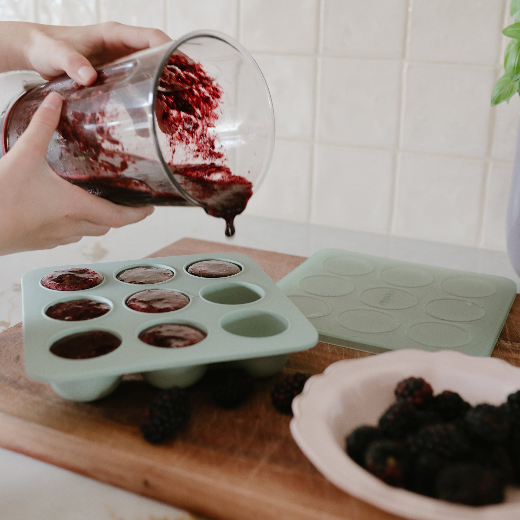 Person pours berry mixture into Mushie Baby Food Freezer Tray with blackberries nearby.