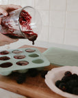 Person pours berry mixture into Mushie Baby Food Freezer Tray with blackberries nearby.