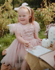 Child in pink dress with pumpkins & mushie Reusable Water Color Pad sits outdoors, smiling.