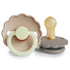 The FRIGG Daisy Night Natural Rubber Pacifier 2-Pack features two pacifiers with scalloped edges in beige/cream and gray, designed for safety and quality—ideal for parents seeking trusted FRIGG products.
