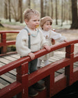 Two kids with FRIGG Daisy Natural Rubber Pacifiers stand on a red bridge in the forest.