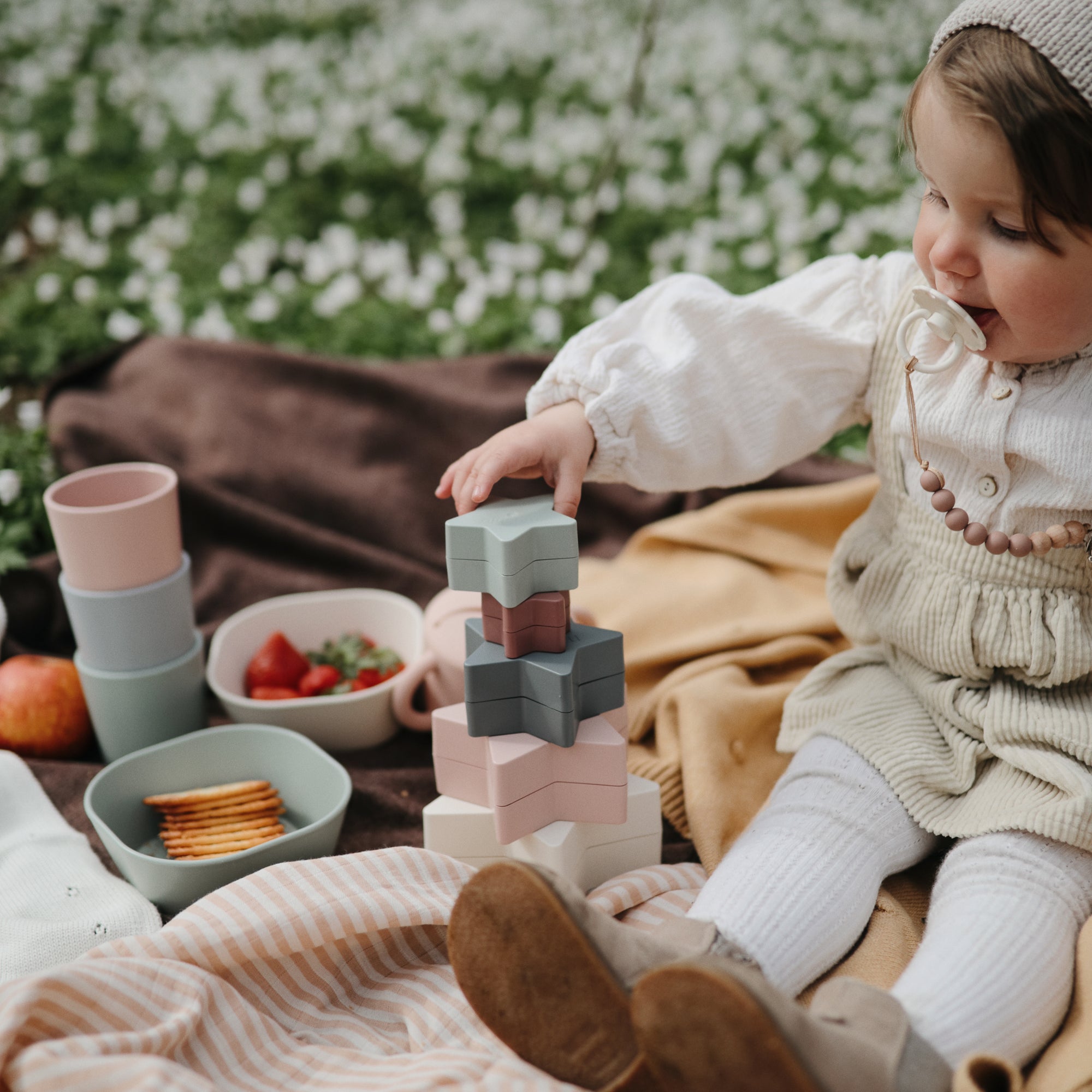 Toddler stacking mushie Nesting Stars Toy on a picnic blanket, building fine motor skills.