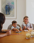 A woman and two kids craft at the table with candles, art, and a mushie Silicone Sensory Toy.