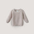 The mushie Chunky Knit Sweater is a light beige, long-sleeve baby sweater made from organic cotton with ribbed cuffs, hem, and neckline, shown on a plain white background.