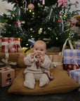 Baby enjoys mushie Teething Ring amid Christmas gifts beneath the festive tree.