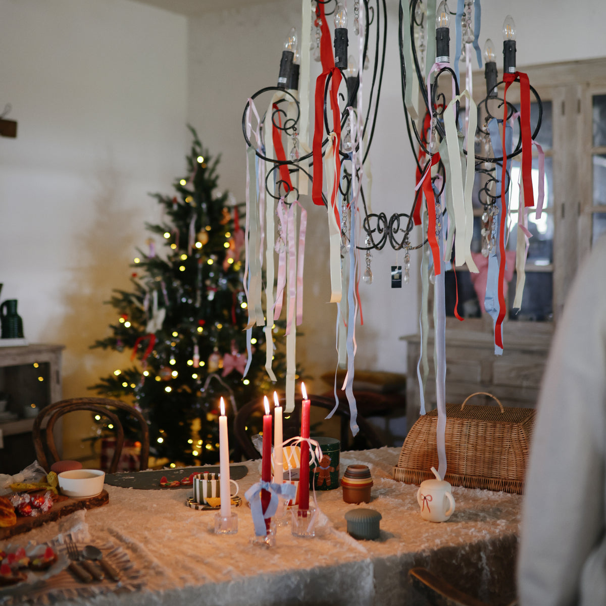 Festive table with Mushie Silicone Training Cup + Straw; Christmas tree lights glow behind.