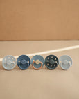 Lifestyle image of a blue-themed line of Frigg pacifiers, featuring the Powder Blue and Slate Moon Pacifiers. 