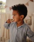 Lifestyle image of a young toddler boy with dark curls and blue striped pajamas holding a Shifting Sand Star Training Toothbrush and brushing his teeth