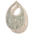 Two mushie Muslin Bibs are shown: one with a green paisley pattern, the other solid beige. Made from organic cotton muslin, both feature rounded edges, snap neck closures, and are layered with the patterned bib on top.