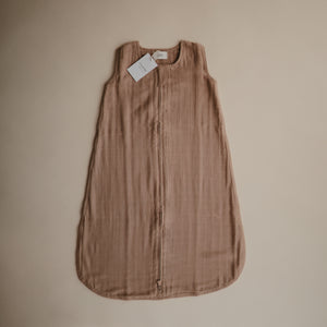 Lifestyle image of a Mushie Sleep Bag in Natural with a tag.