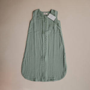Lifestyle image of a Mushie Sleep Bag in Roman Green with a tag.