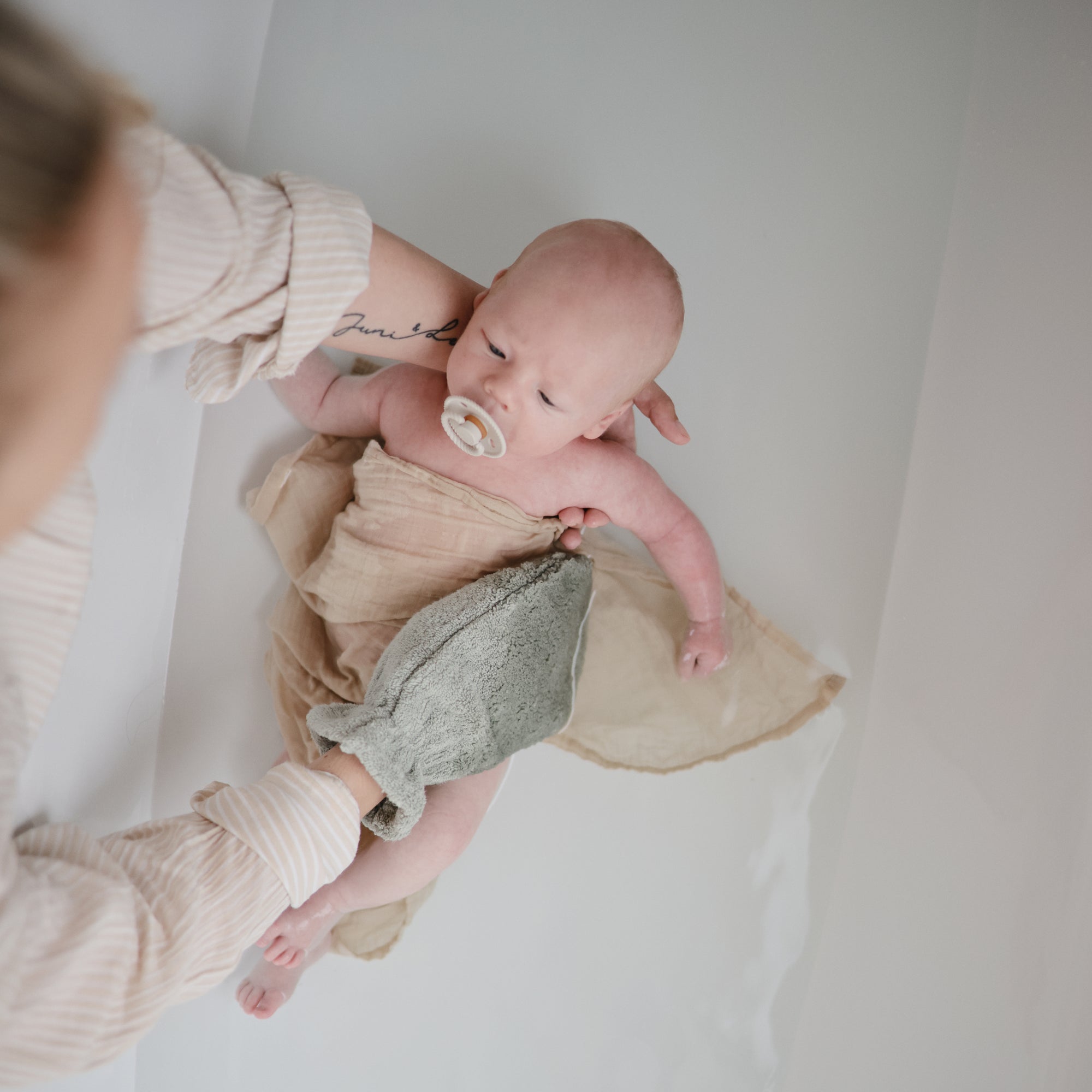 Lifestyle image of a mom using a bath mitt to clean a baby in a shallow tub.